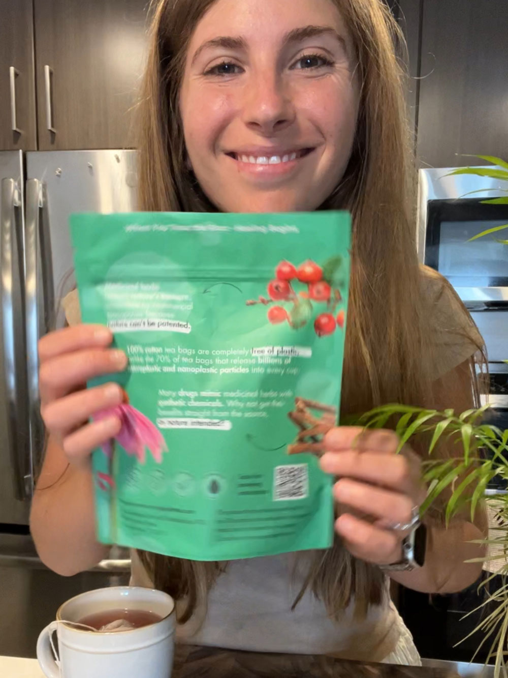 Customer with a SingularTea personalized herbal remedy pouch (back label) and a brewed cup on the counter.