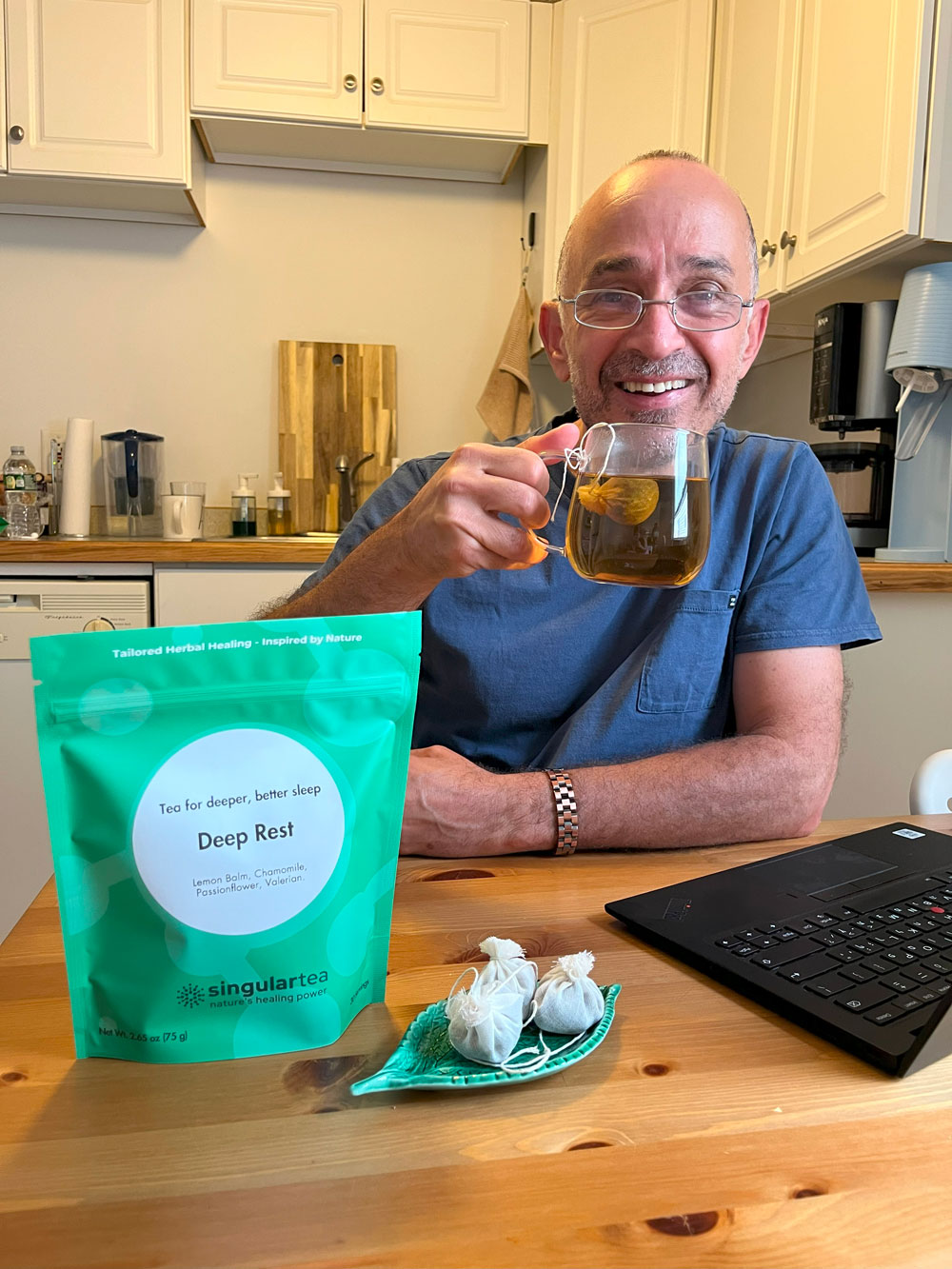 Customer holding a hot cup; SingularTea personalized remedy pouch and two premium cotton tea bags on the table.
